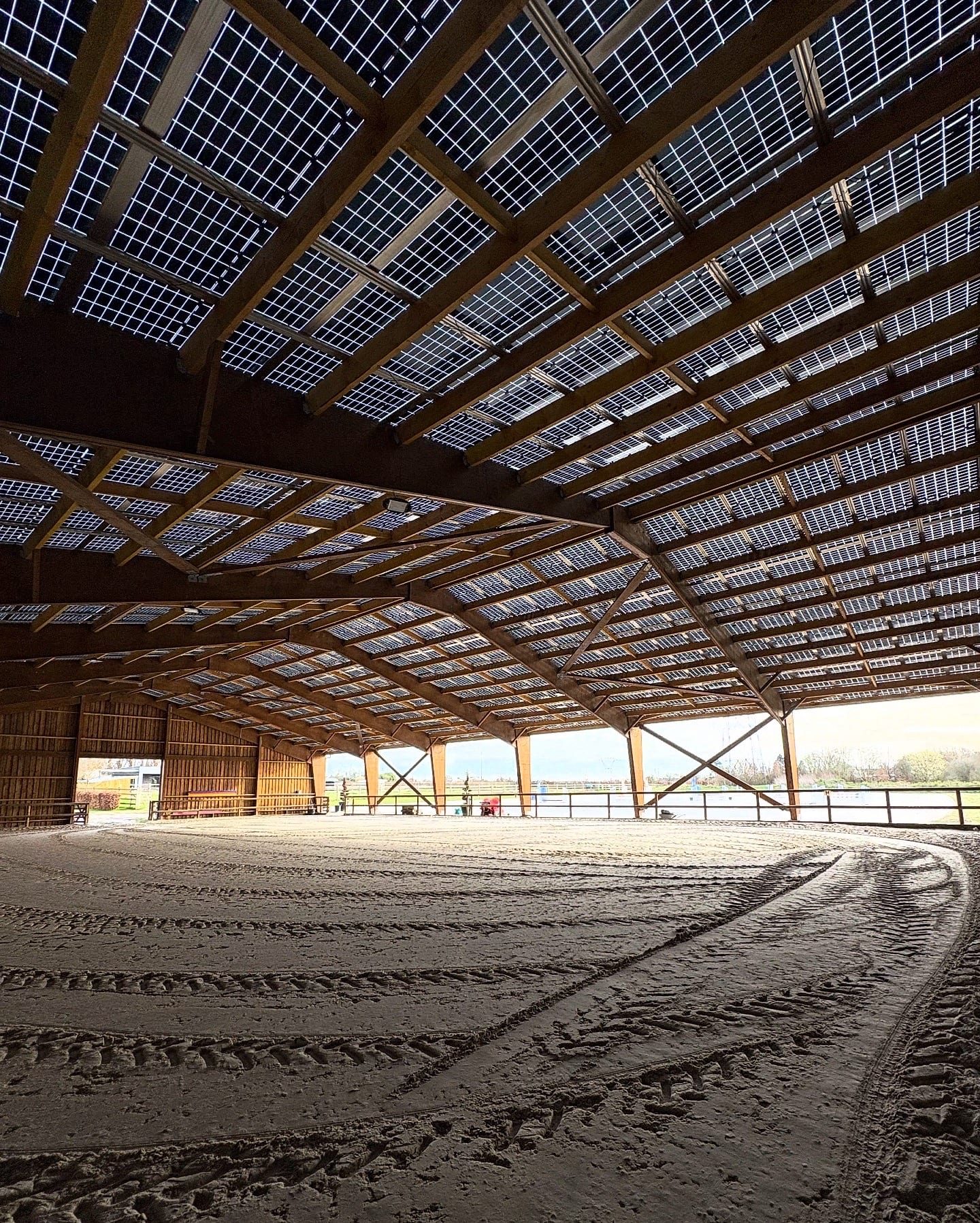 Vaste manège couvert au sol sablé sous une toiture en panneaux photovoltaïques.